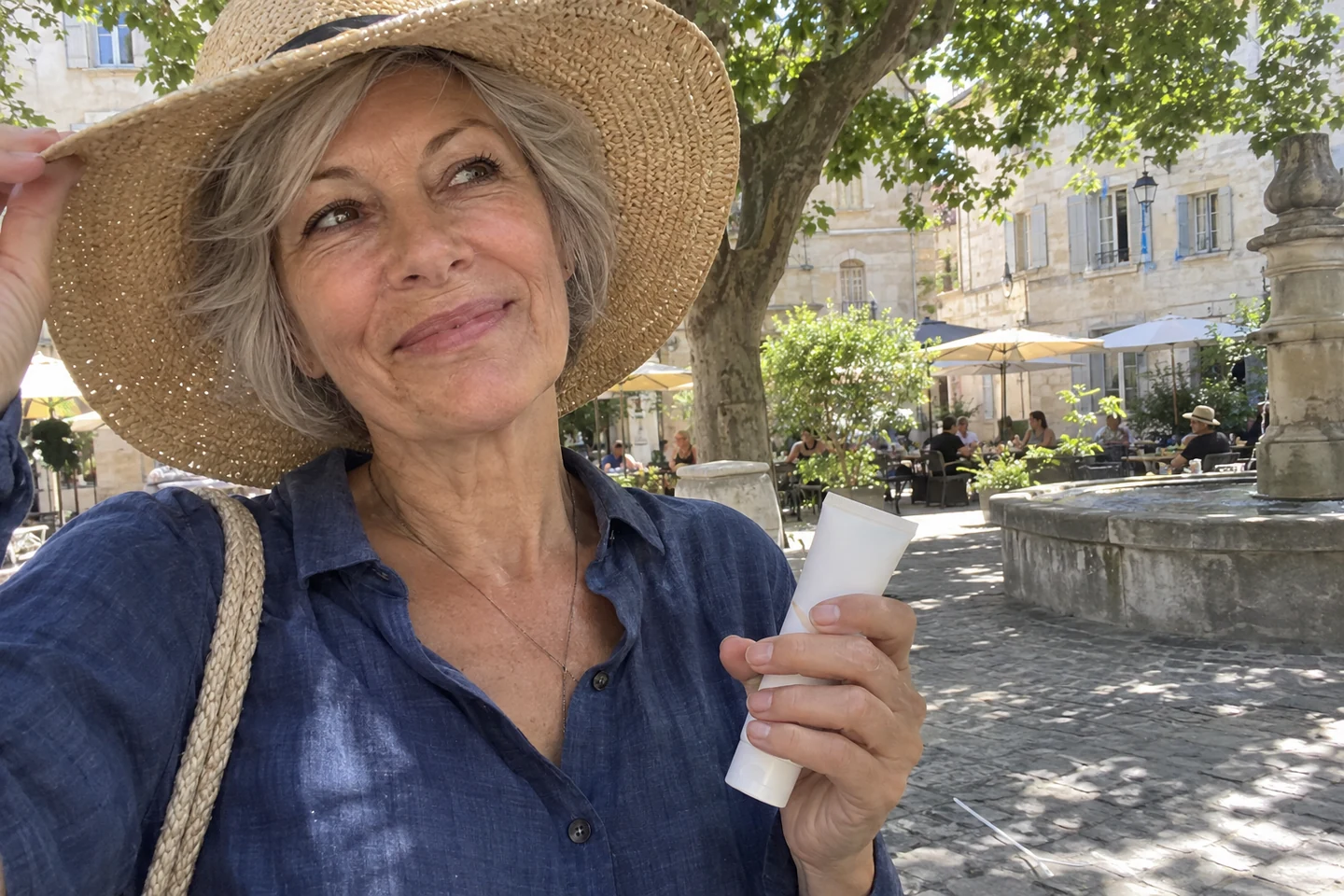 Une femme porte un chapeau et tient son écran solaire à l’ombre d’une place