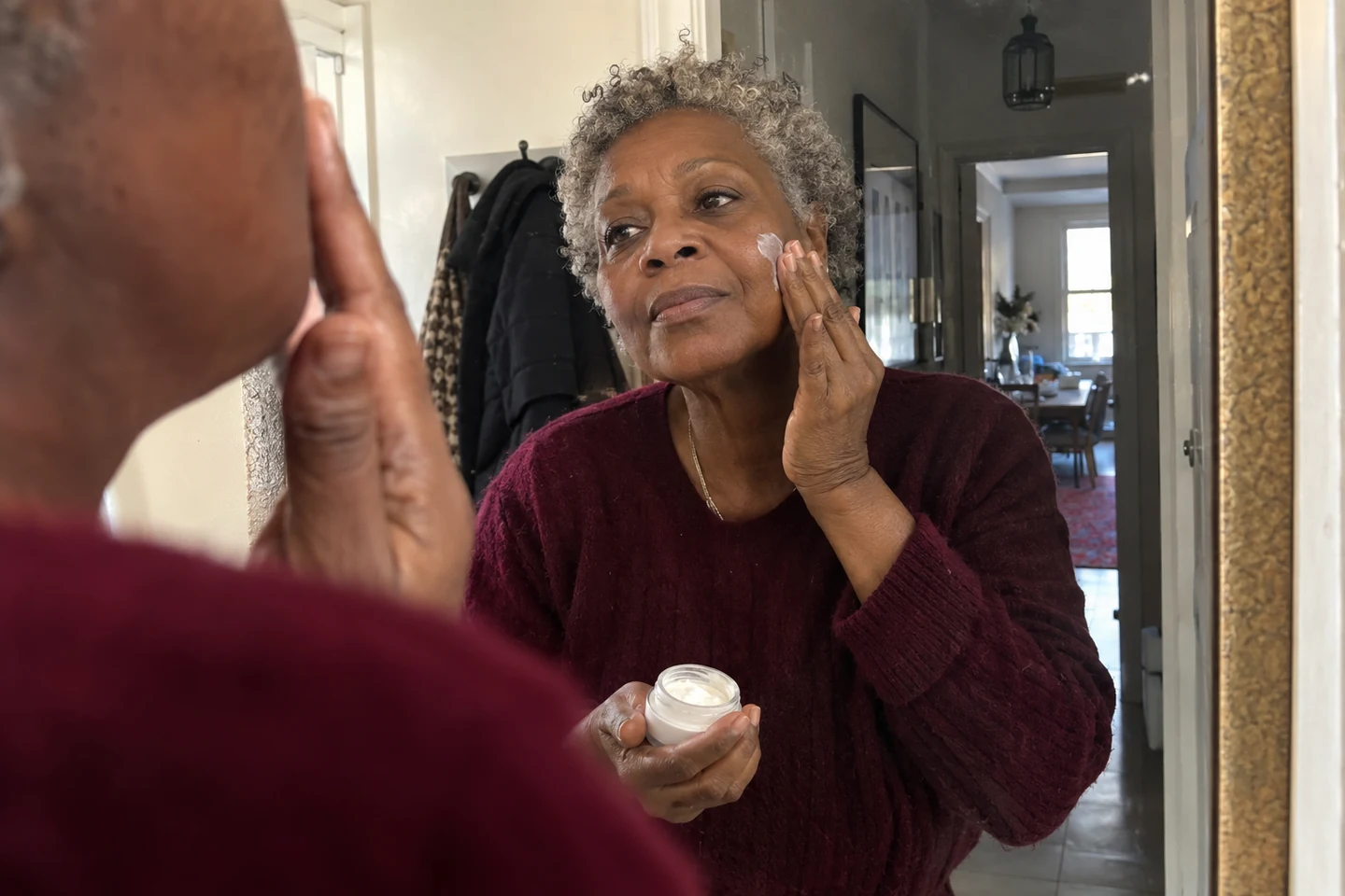 Une femme applique une crème devant le miroir de sa salle de bain