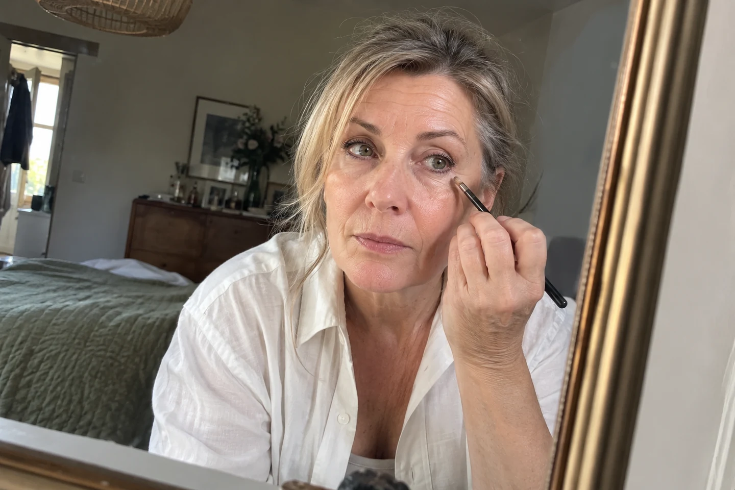 Une femme observe son maquillage des yeux dans un miroir