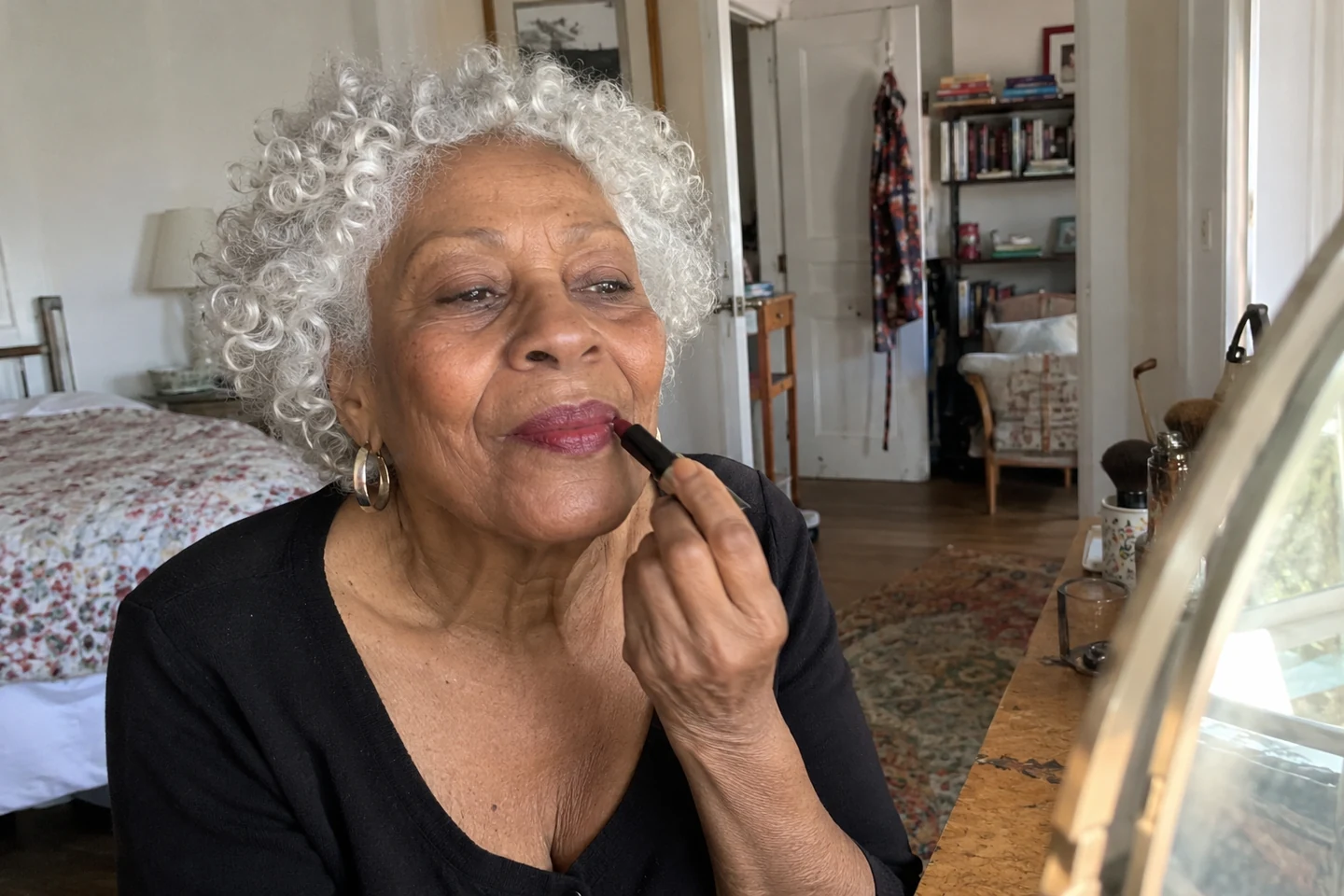 Une femme aux cheveux blancs bouclés applique un rouge à lèvres