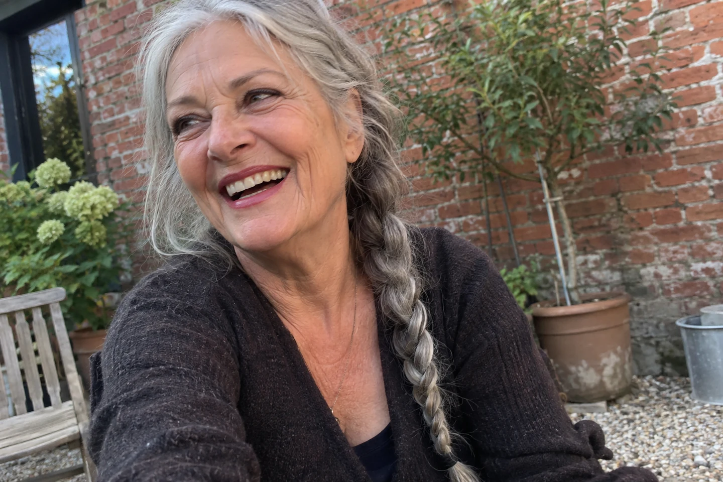 Une femme aux cheveux gris rit dans une cour plantée