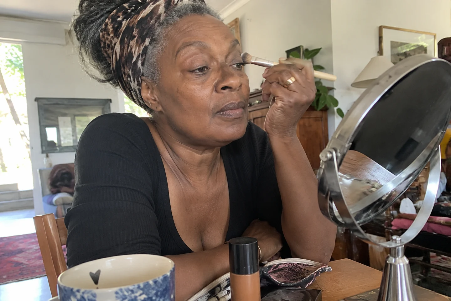 Une femme ajuste son maquillage avec un appui du coude sur la table