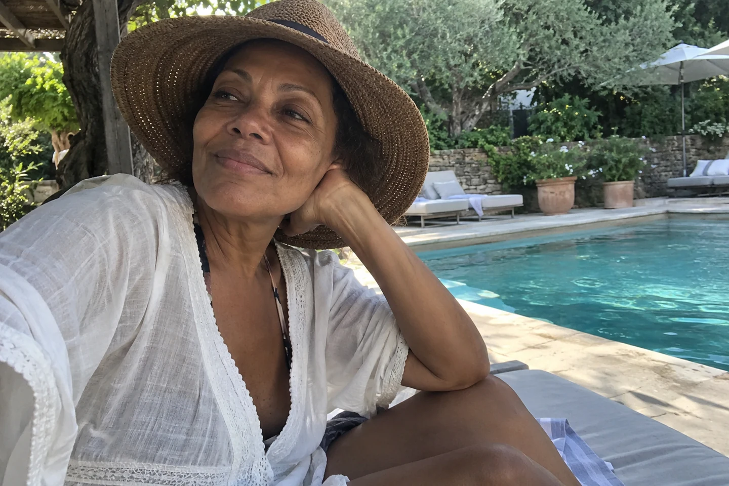 Une femme porte un chapeau à l’ombre près d’une piscine extérieure