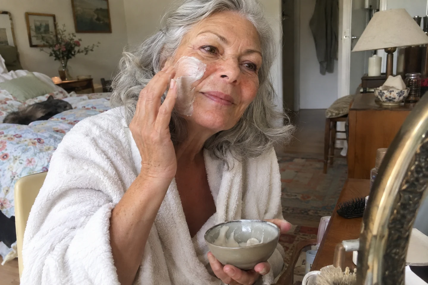 Une femme applique un masque crème sur sa joue devant un miroir
