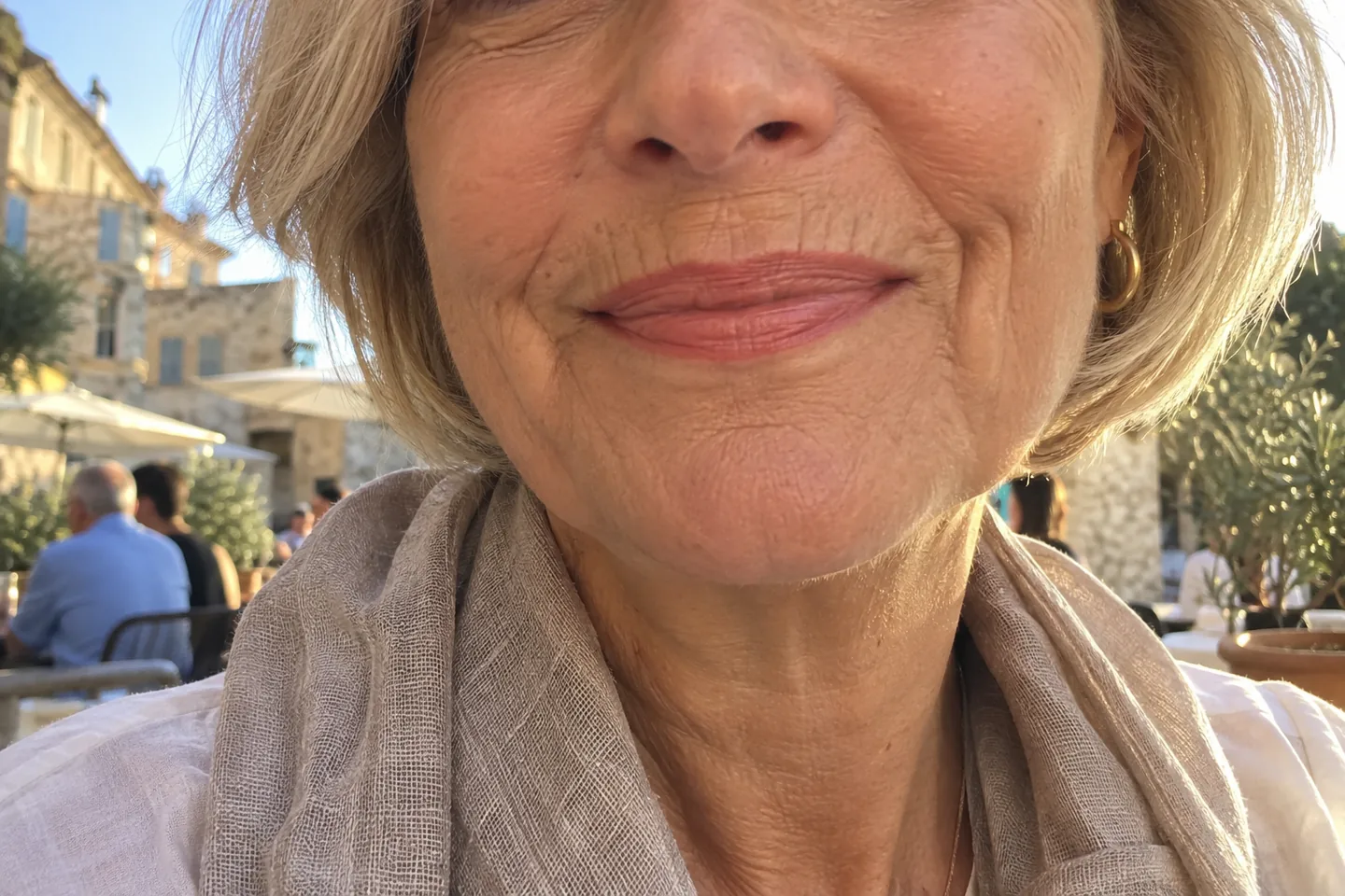 Bas du visage d’une femme de 62 ans souriante en terrasse, ridules visibles au-dessus de la lèvre