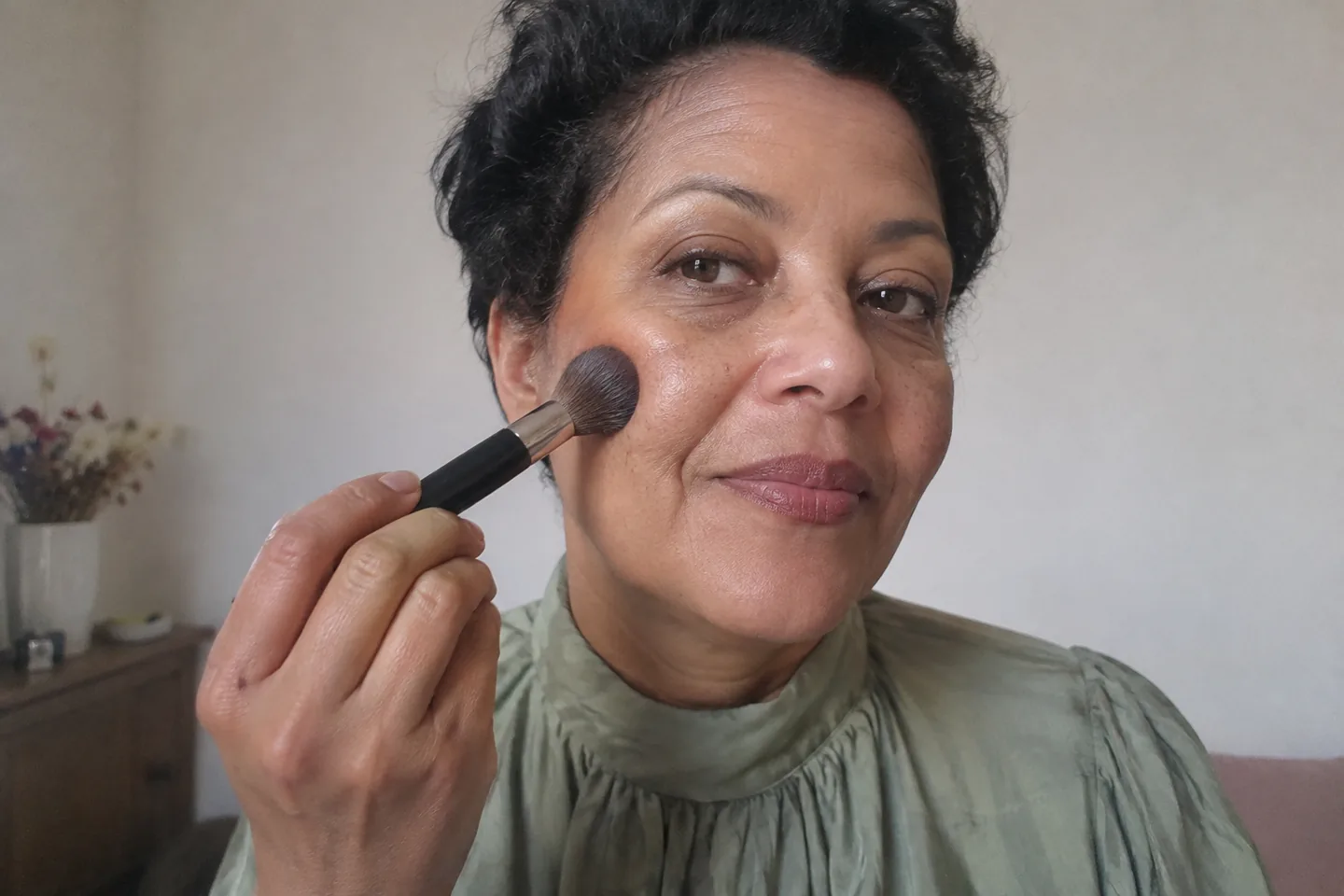 Femme appliquant une petite quantité de maquillage au pinceau sur une joue