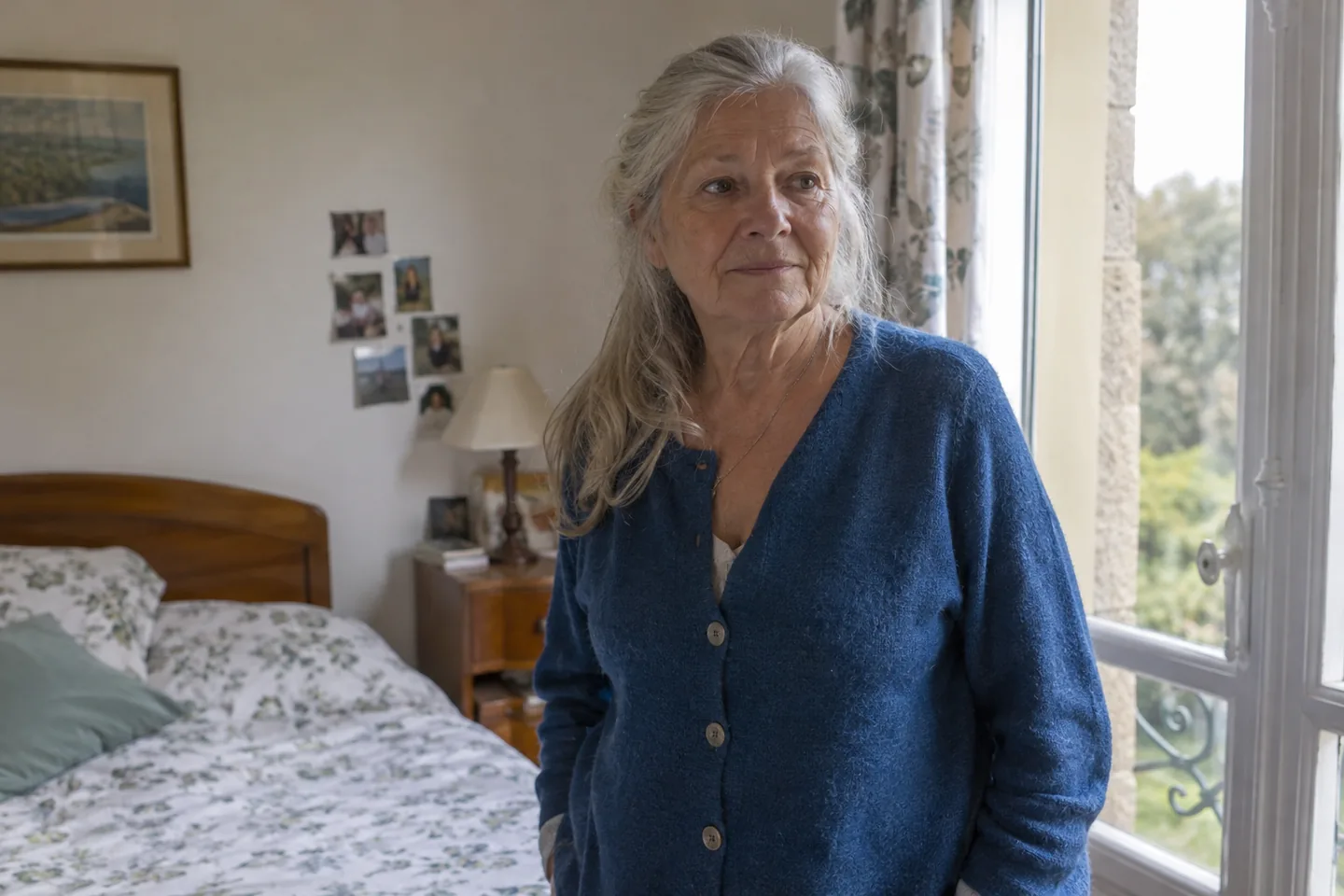 Femme aux cheveux gris debout près d’une fenêtre