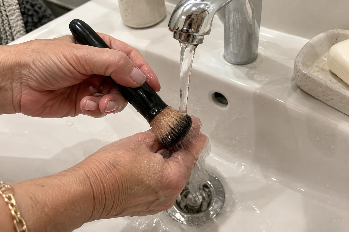 Mains lavant les poils d’un pinceau sous un filet d’eau